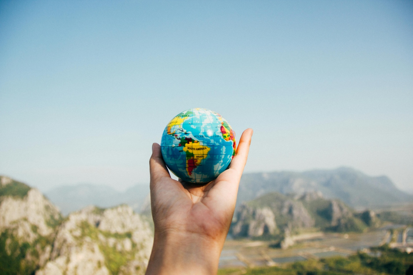 A person holding a tiny globe while facing mountains