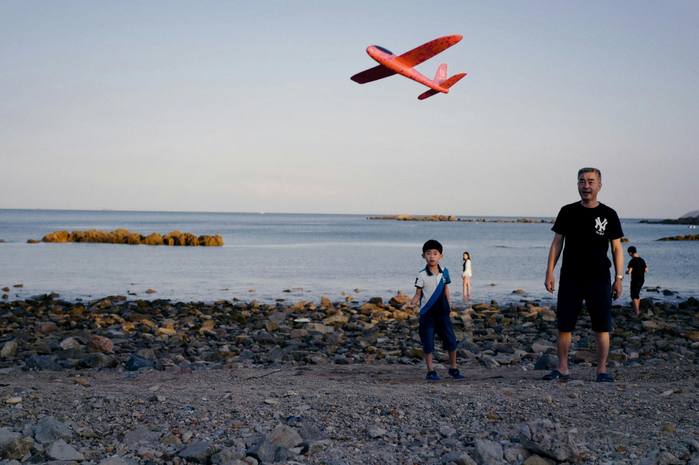 A father and son playing with a toy plane by the shore. 